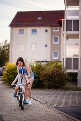 Mother Helping Son Learn to Ride a Bike on Sidewalk