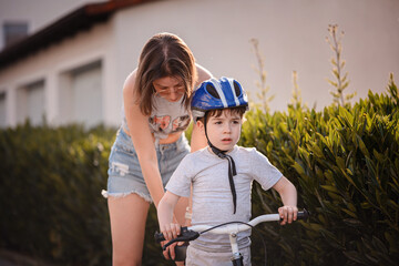 Mother Supporting Young Boy Learning to Ride a Bike