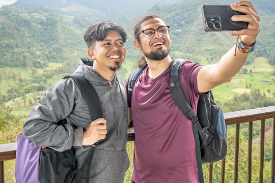 Two Latino men taking a selfie amidst a mountainous landscape. Two young happy men friends hikers taking a selfie in the mountain