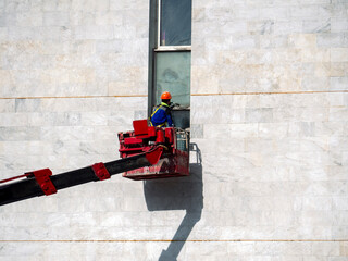 High-rise works on the facade of a building from an aerial platform. Reconstruction and repair of windows and walls. A construction worker is repairing a window from an aerial platform.