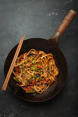 Wok pan with stir fry chicken and vegetable noodles, with wooden chopsticks resting on top, top...