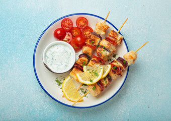 Grilled chicken skewers seasoned with herbs and spices, served on a plate with lemon wedges, cherry tomatoes and yogurt sauce, flavorful and healthy meal mediterranean style on blue background