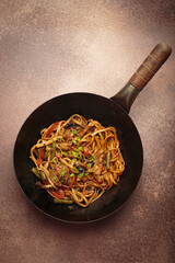 Wok pan with stir fry chicken and vegetable noodles, with wooden chopsticks resting on top, top...