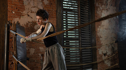 Short-haired boxer pausing workout, leaning on ring ropes with cinematic intensity