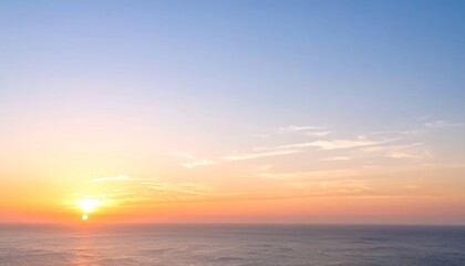 Fototapeta premium Blurry sunset over ocean. Soft colors of orange, pink, and blue in the sky. Gentle clouds. Ocean surface below is hazy