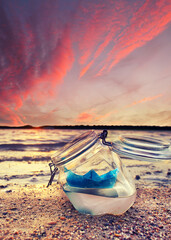 Sailing Serenity: A Blue Paper Boat in a Glass at Autumn Sunset