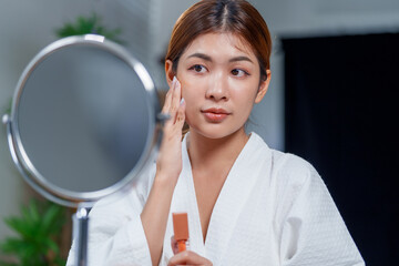 Woman in bathrobe applies makeup while looking in mirror, showcasing her beauty and confidence....