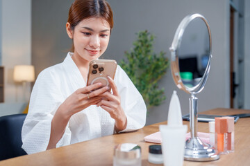 Woman in bathrobe is sitting at vanity, applying makeup while looking at her phone. scene captures beauty and cosmetics in serene setting