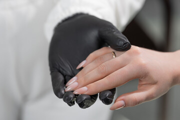 Close-up of manicure master applying light beige gel polish to elegant almond-shaped nails in salon