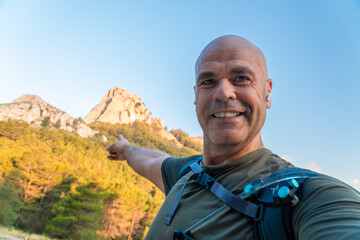 Hiker looking at camera and pointing a mountain on background