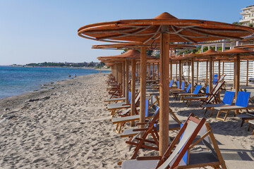 A bay on the southern coast of Italy with clear blue sea, mountains in the background and a sandy beach surrounded by colorful umbrellas and sun loungers.