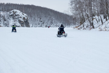 Two people are riding snowmobiles on a snowy road