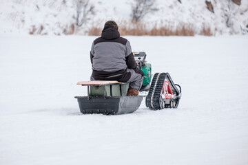 A man is sitting in a snowmobile with a man in a snow suit sitting in a sled beh