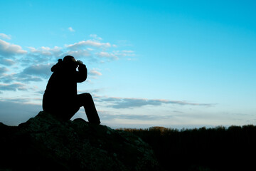 the silhouette of a man on a stone looks into the distance