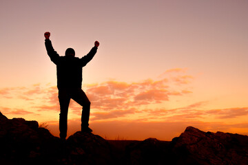 A man is standing on a rock with his arms raised in the air