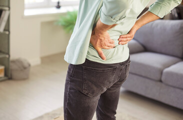 Cropped portrait of man suffering from backache standing in living room at home. Male person in...