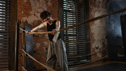 Short-haired boxer pausing workout, leaning on ring ropes with cinematic intensity