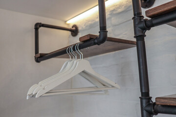 Close-up of white wooden clothes hangers on a black metal rod with dark wood shelves mounted on a...