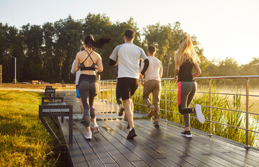 Back view of a team of young people running together in summer park having sport workout outdoors....