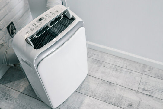Close-up of a portable air conditioner with digital display and control panel, placed on a wooden floor near a wall socket