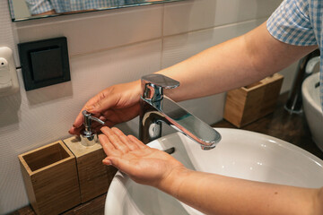 Close-up of a person pressing a soap dispenser in a modern bathroom with a white sink and bamboo...