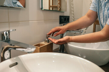 Close-up of a person pressing a soap dispenser in a modern bathroom with a white sink and bamboo...