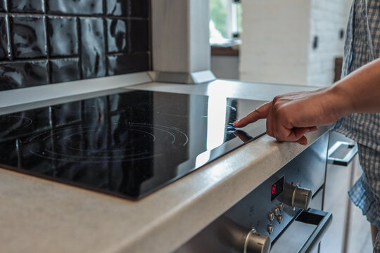 Close-up of a person turning on a modern induction cooktop with a touch control panel in a bright kitchen interior