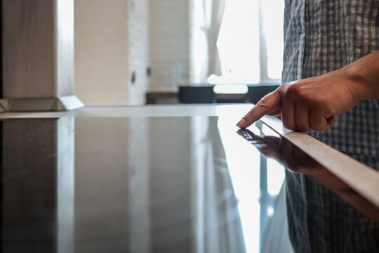 Close-up of a person turning on a modern induction cooktop with a touch control panel in a bright kitchen interior
