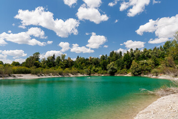 Turquoise lake with pebble shore and clear water, surrounded by forest and blue sky – perfect for...