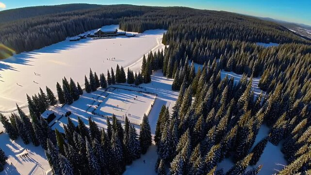 peaceful drone view over a winter ice skating scene on a frozen lake in Evergreen Colorado with bright morning sun reflecting on smooth ice surrounded by lodge and snow covered golf course