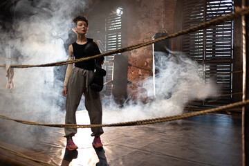 A woman in a boxing gym, portrait by the ropes, cinematic style, dark tones. Training and...