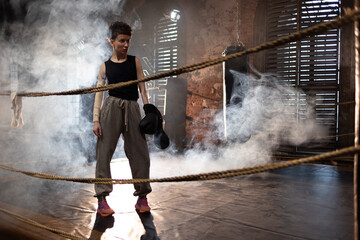 A woman in a boxing ring, holding boxing gloves in her hands, preparing for boxing training. The...