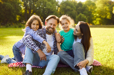 Portrait of happy smiling family with son and daughter sitting on green grass in the summer park...