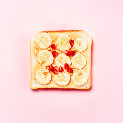 Toast with banana slices and pomegranate seeds on a pink background.