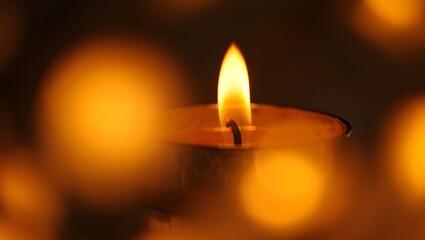 Close up of a single lit candle flame with soft blurred bokeh lights in the background creating a warm and inviting atmosphere