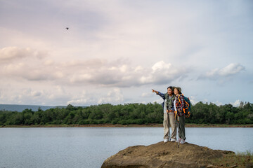 Two people standing on a rock overlooking a body of water. One of them is pointing at a bird flying in the sky