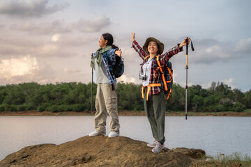Two women are standing on a rock by a lake. One of them is wearing a hat. They are both smiling