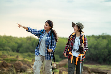 Two women are walking in the woods. One of them points to the sky. They are wearing backpacks