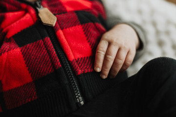 Close-up of baby wearing red and black buffalo plaid fleece vest with visible hand resting on warm...