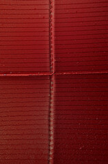 Close-up macro photo of a textured red paper surface featuring a prominent cross-shaped fold or seam. The paper shows fine horizontal lines and subtle surface grain.