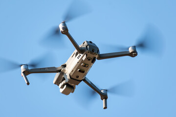 A drone flies in a blue sky with white clouds. A close-up of a drone with a lens filter activated, flying in sunny daylight. A new quadcopter hovers against a light blue background.