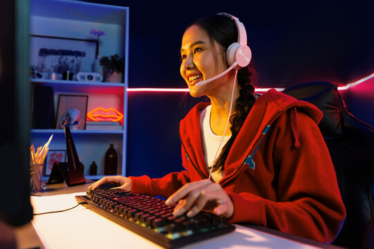 Host channel of smiling beautiful Asian girl streamer playing online game wearing headphone talking with viewers media online recording phone. Esport skilled team players in neon blue room. Stratagem.