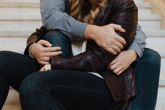 Close-up of couple sitting on stairs embracing warmly with intertwined arms, casual clothing including jeans and leather jacket, suggesting intimacy, love, and relationship connection