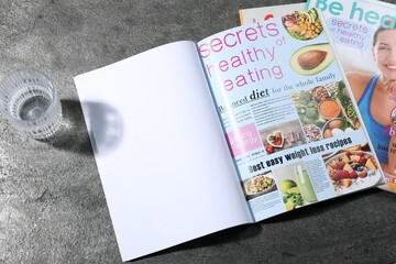 Trendy magazines and glass of water on grey background. Mockup for design