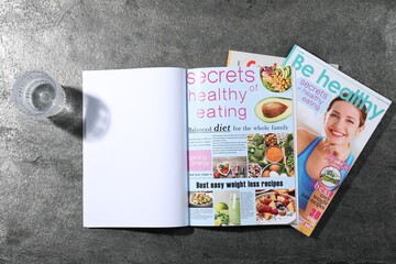 Trendy magazines and glass of water on grey background, top view. Mockup for design