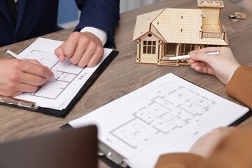 Real estate agent working with client at desk with house model in office, closeup