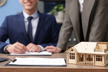 Real estate agent working with client at desk in office, focus on house model