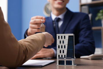 Real estate agent giving key to client at desk in office, focus on house model