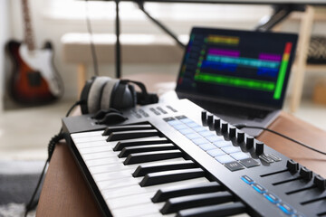 MIDI keyboard, laptop and headphones on wooden table in home studio, selective focus