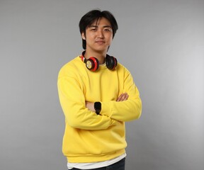 Handsome Asian man with headphones on grey background